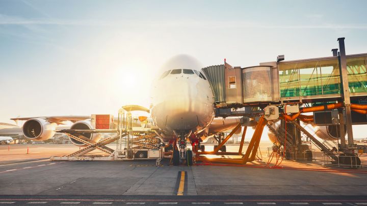 An airplane at a gate in an airport, with bright sunlight illuminating the scene.